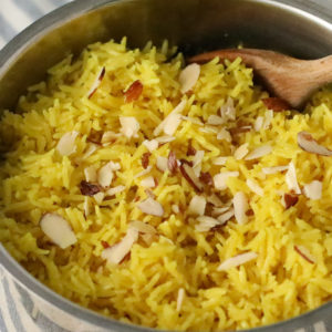 tumeric coconut rice in a stainless steel pot with a wooden spoon